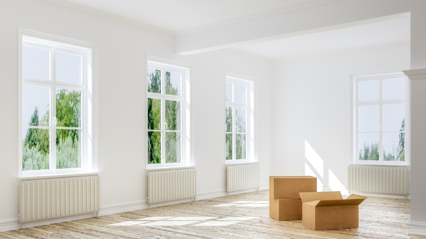 Sala luminosa y vacía con suelo de madera y unas cajas de cartón preparadas