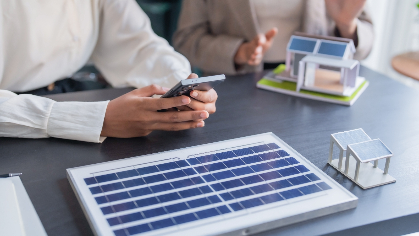 Reunión de trabajo con una placa solar, una maqueta de vivienda y un teléfono sobre la mesa